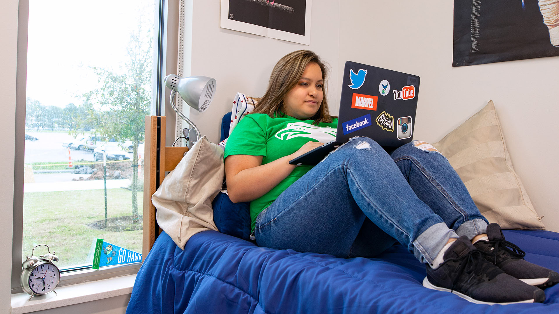 Student studying in a Hunter Residence Hall dorm room by a sunny window.